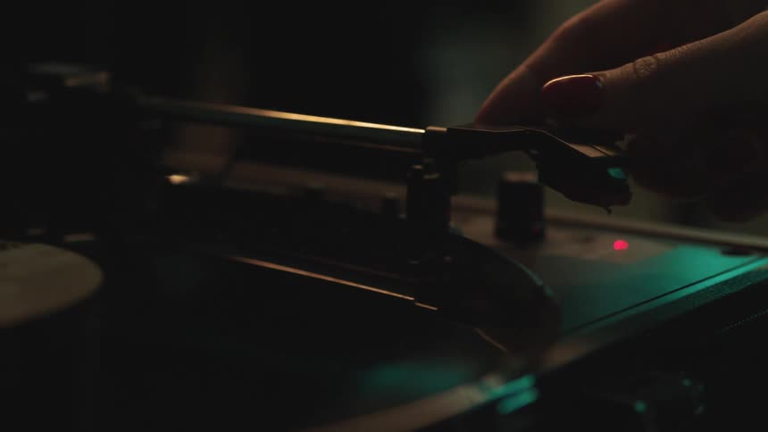 Hand moving a turntable needle over a vinyl record in a dimly lit room