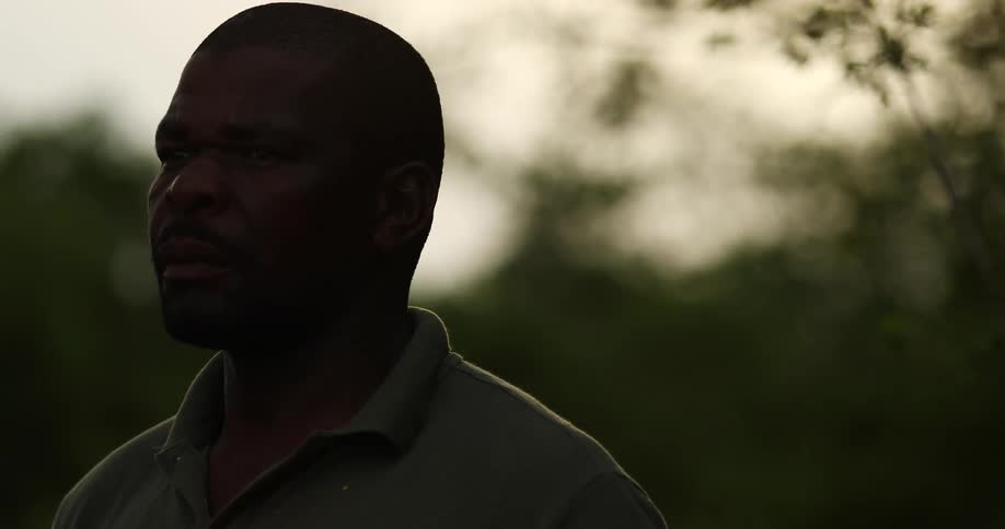 Black man in polo shirt stands outside looking contemplatively into distance