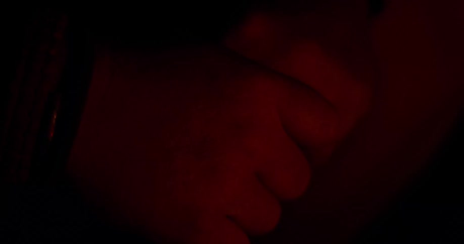 Person clasps and reclasps hand under flickering red tinted light
