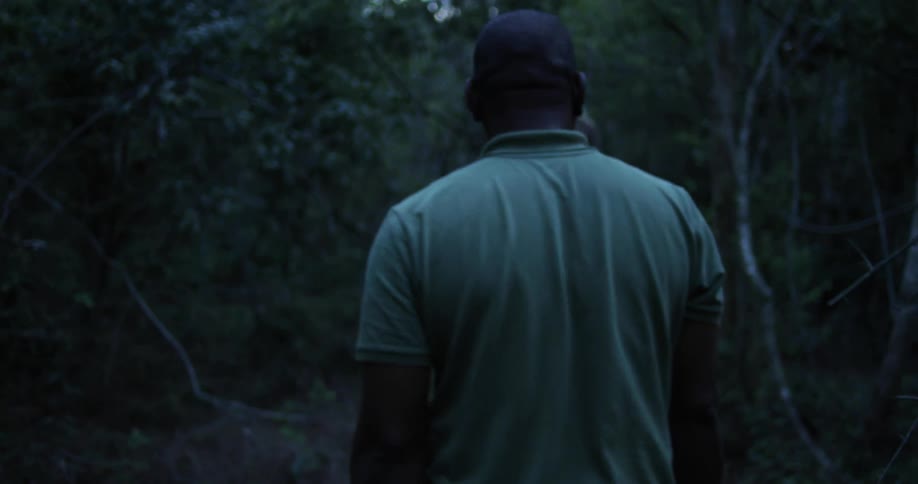 Two men walk through a heavily wooded area with a shot gun