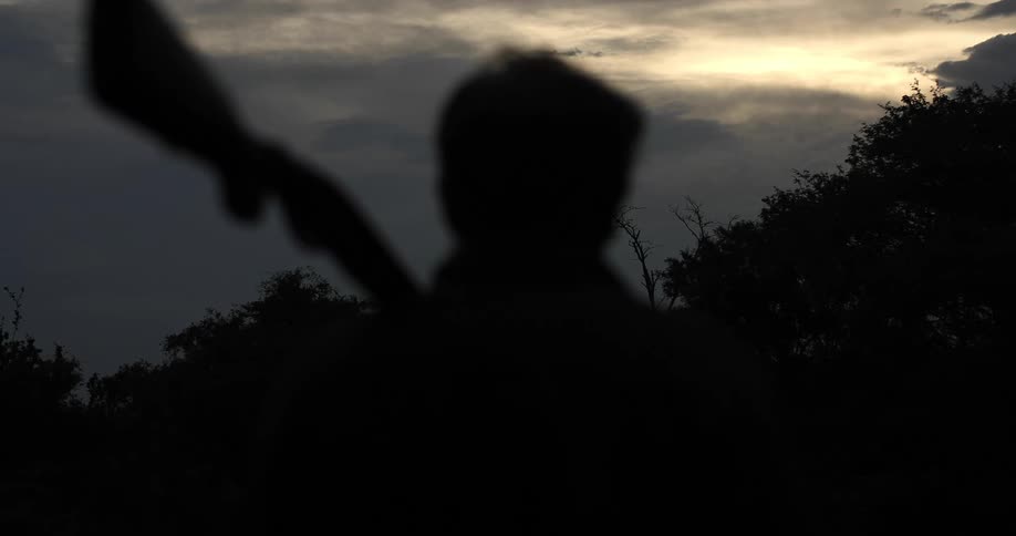 A person stands in the shadows with a rifle