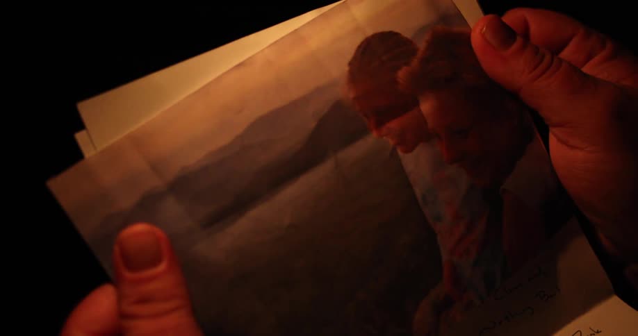Man sitting by a campfire reads a letter and then looks at a photograph