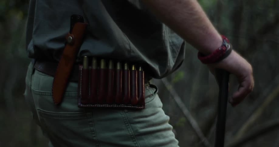 An outdoorsman has a knife and ammunition on his belt
