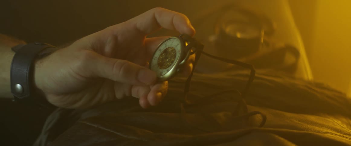 Person picks up and examine watch hanging on cord in dim room