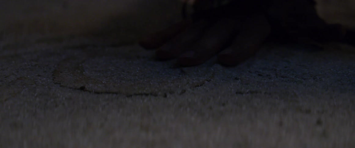 Hand brushes sand away from symbol on ground