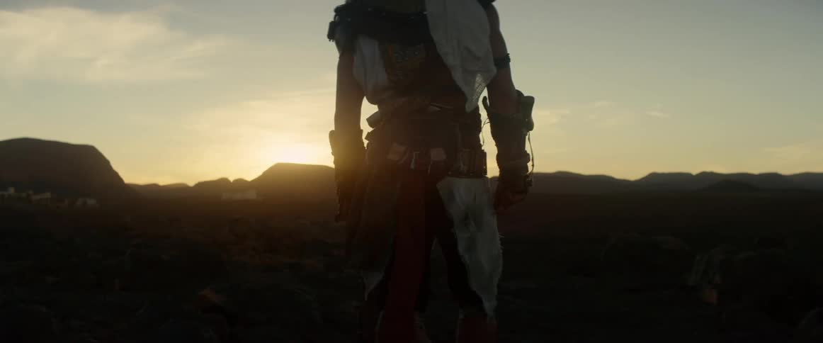 A man is standing in rugged terrain watching the sun rise