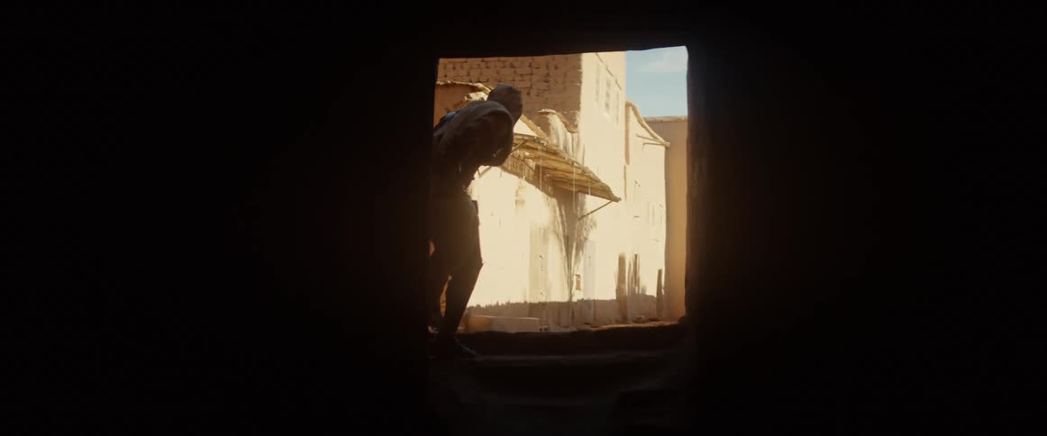 A person emerges from the shadows and moves quickly through the daylight
