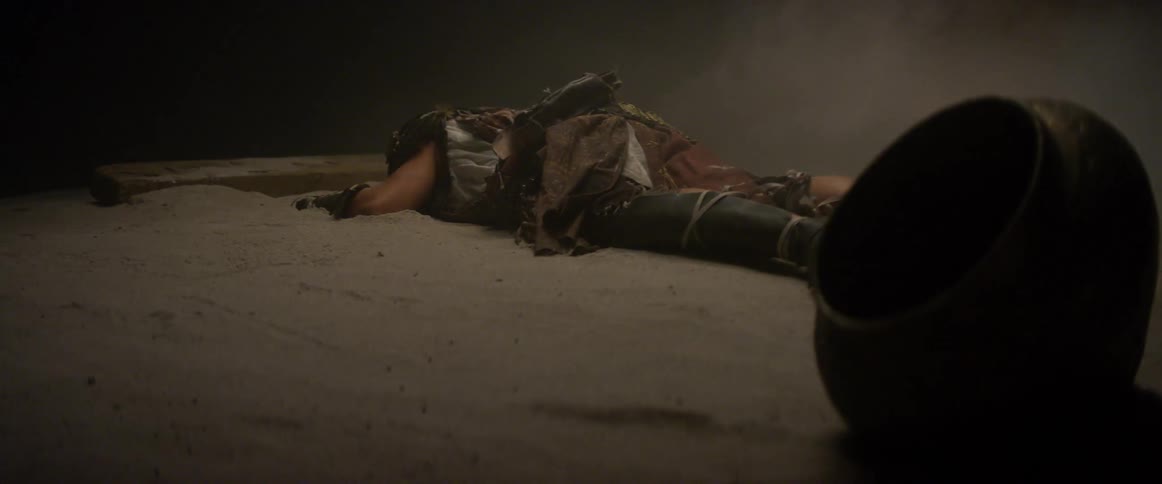 A person laying on the sand next to a vase and a plank of wood