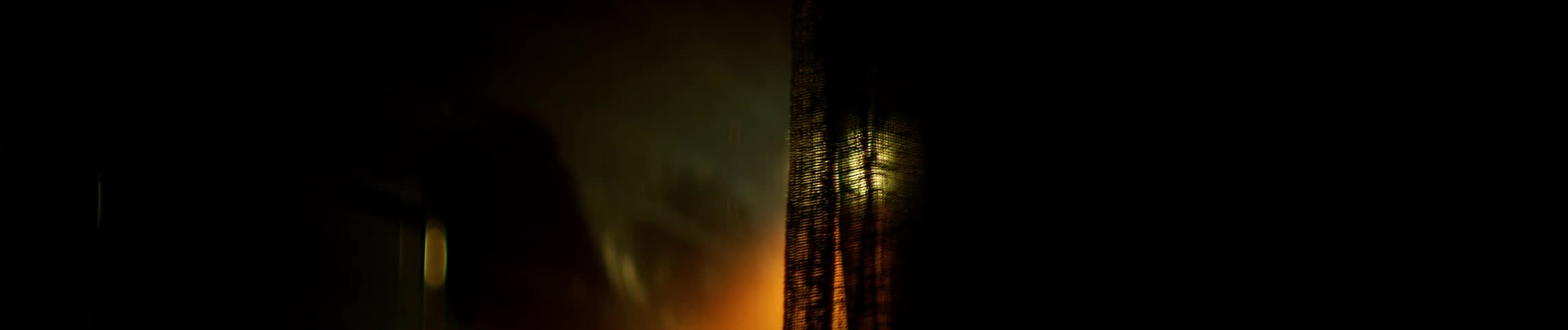 Curtains hang in the window as a bright light shines in the distance