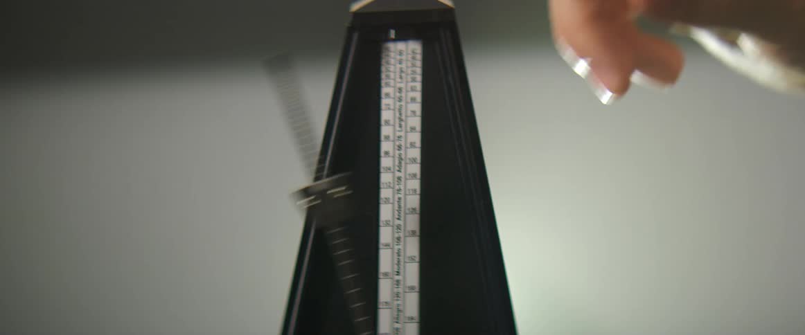 A white person flicks a metronome to get it to start moving