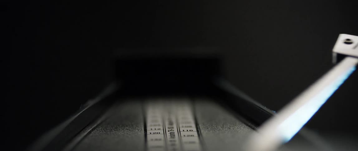 A metronomes arm swings against a dark background