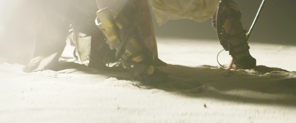 A bright light strongly flashes as a man in costume kneels in the sand