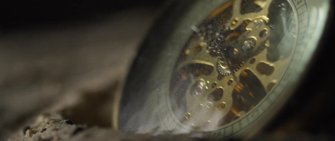 A pocket watch sits in sand in the desert