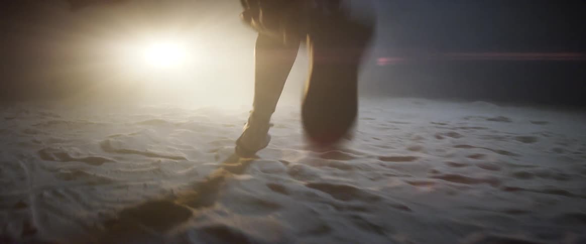 A person running with boots on sand towards a light
