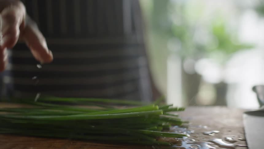 Man places fresh green onion leaves on a cutting board in the kitchen