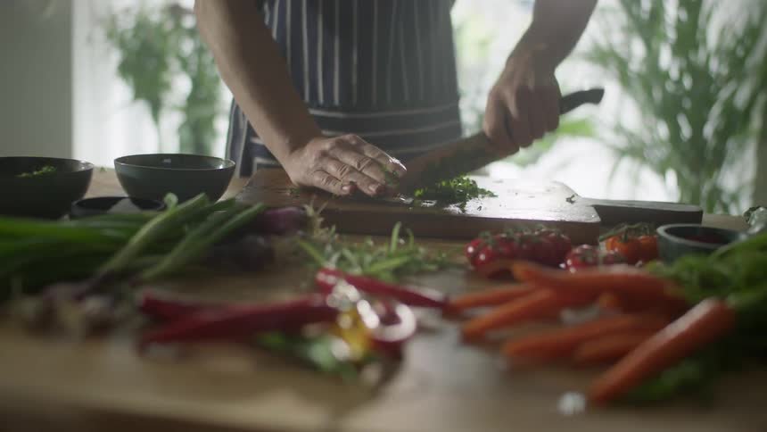 A person in a striped apron chopping vegetables on a wooden cutting board