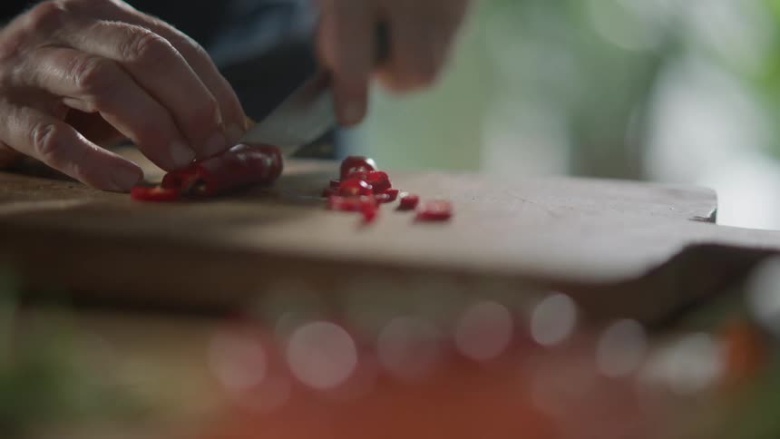 Man cuts red peppers over a cutting board with a sharp kitchen knife