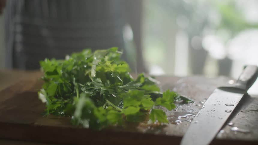 Person throws fresh herbs on a cutting board in the kitchen