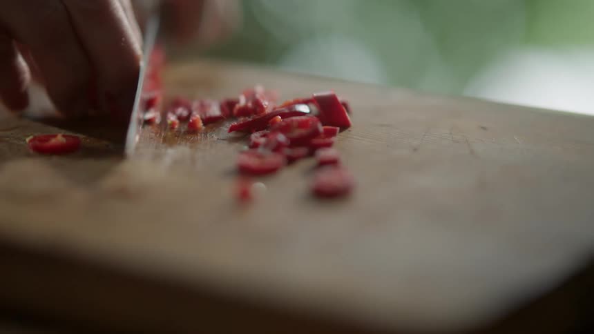 Man finely chops and slices red chili pepper with a sharp kitchen knife on a cutting board