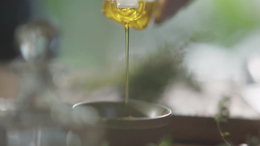 Clear yellow cooking oil pours from a glass bottle into a container in the kitchen