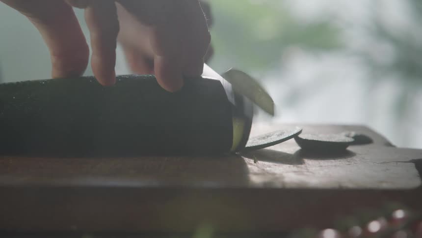 A man cuts a cucumber over a cutting table with a sharp kitchen knife