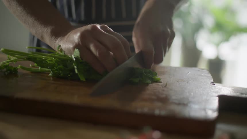 A person uses a knife and chops fresh herbs on a cutting board