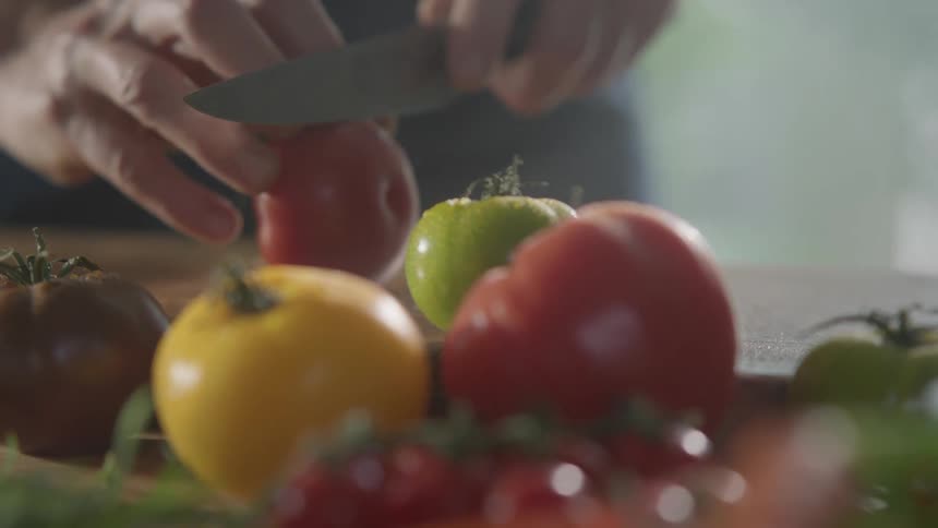 A person picks up a knife and slices through a tomato
