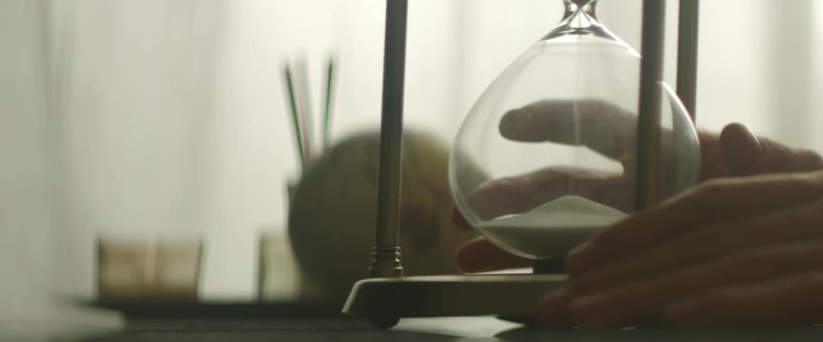A woman taps an hourglass as the sand falls