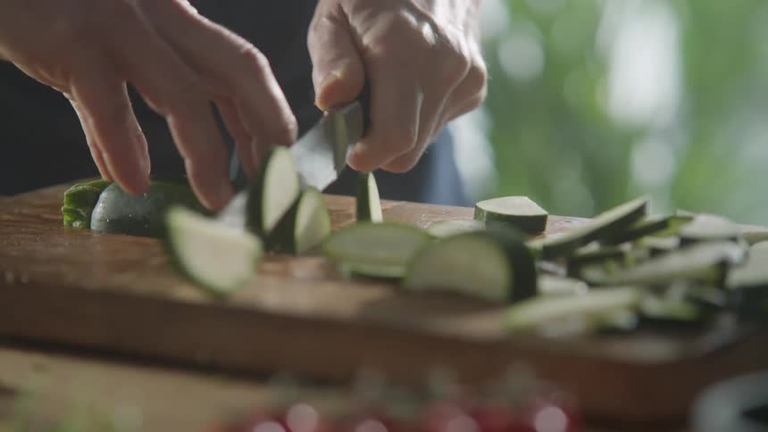 Cucumber is sliced with a sharp knife on a wooden cutting board