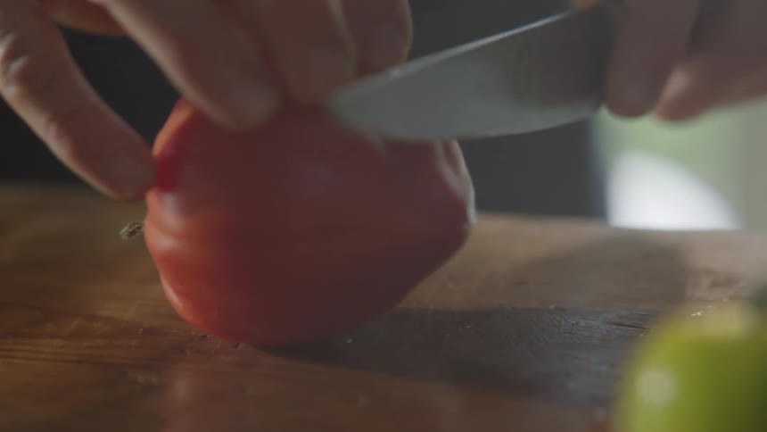 Picking up a red tomato then start slicing it