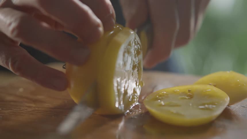 Man cutting a yellow tomato with a sharp kitchen knife over a cutting board in the kitchen