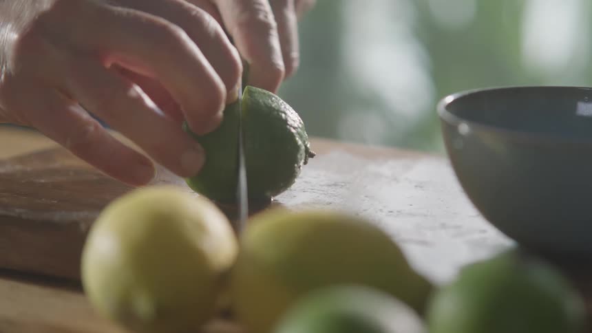 Man cuts a lime in half with a sharp knife in the kitchen