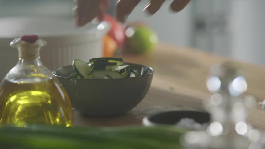 Man places cucumber slices inside a bowl in the kitchen