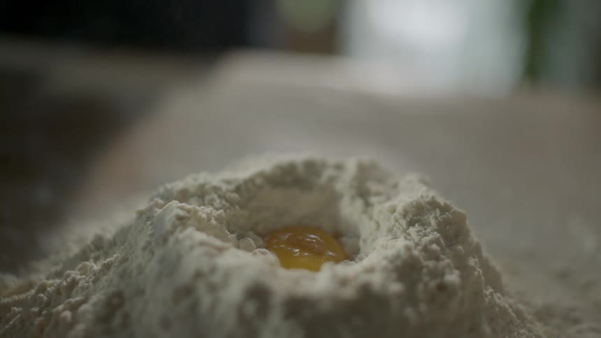 Egg yolk dropping into a hole in a mound of flour