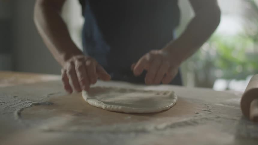 Man kneads flour dough on a table in the kitchen