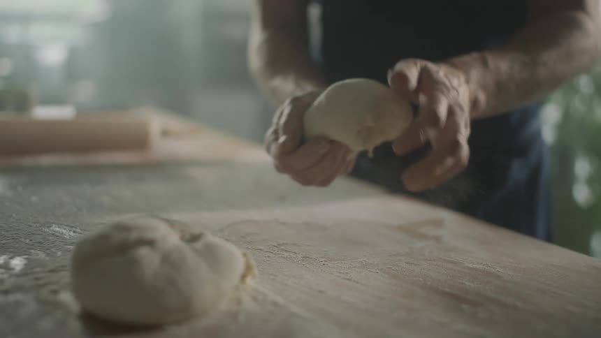 Man with a black shirt kneads bread dough in the kitchen