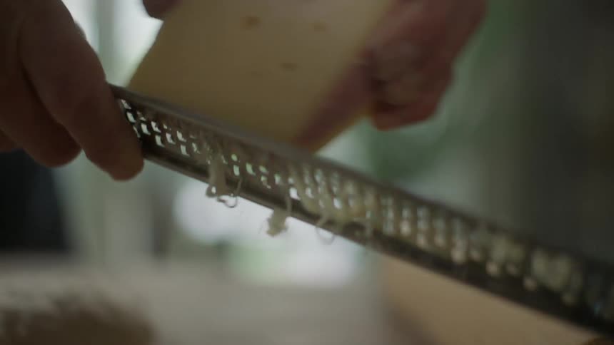 Man grates cheese with a grater in the kitchen