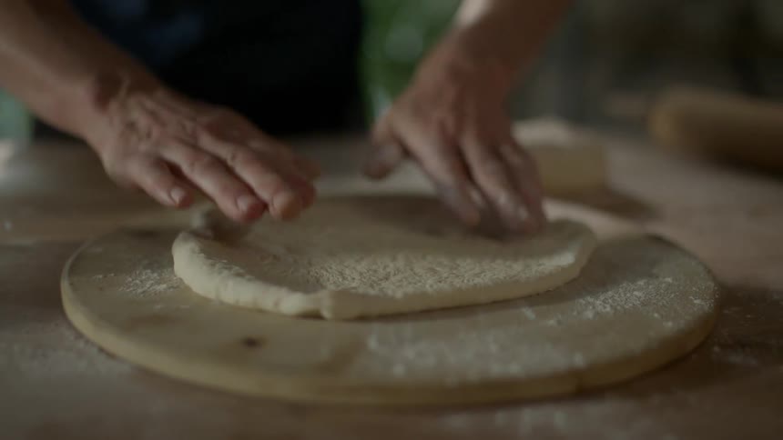 Person puts pizza dough on pizza wheel patting it
