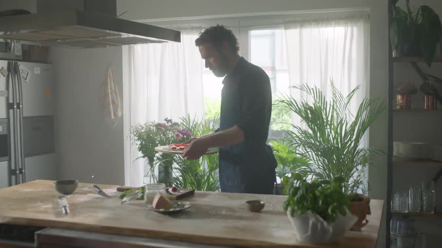 Man wearing apron makes homemade pizza in the kitchen