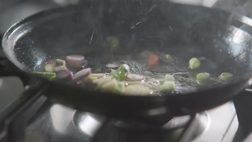 Vegetables being dropped in a pan over a flame