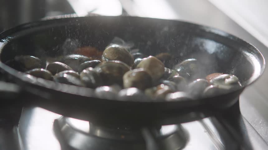 A handful of escargot is added to a saute pan with vegetables in hot oil