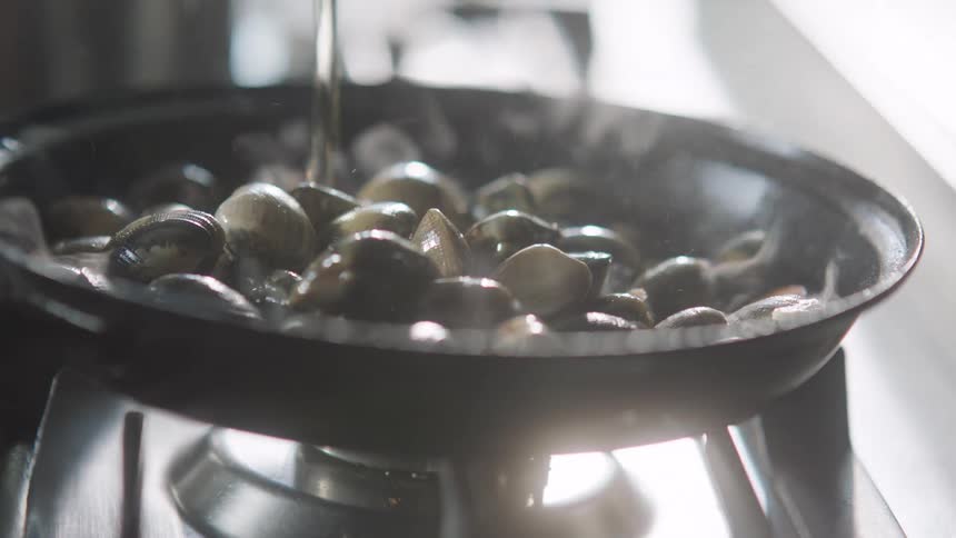 Water pours over clams in frying pan on stove