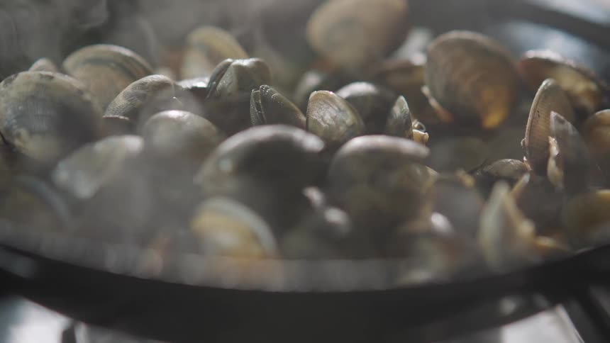 Steam rises from mussels being cooked in a pan