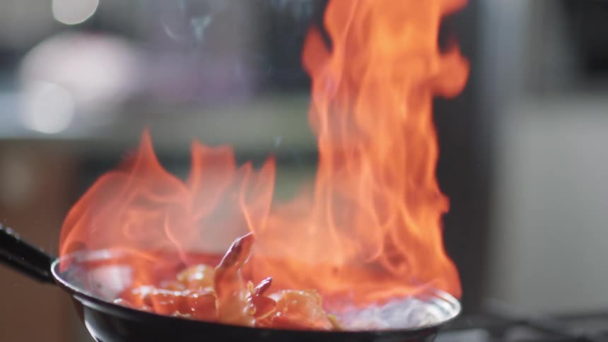 Flames coming off of food as it is being shaken in a pan as it cooks