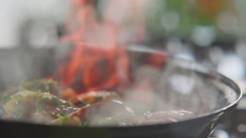 Flames engulf the vegetables being tossed in a pan
