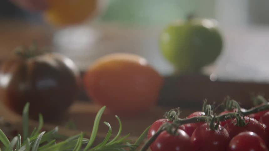 Man picks up a yellow tomato and cuts it with a sharp kitchen knife on a cutting board