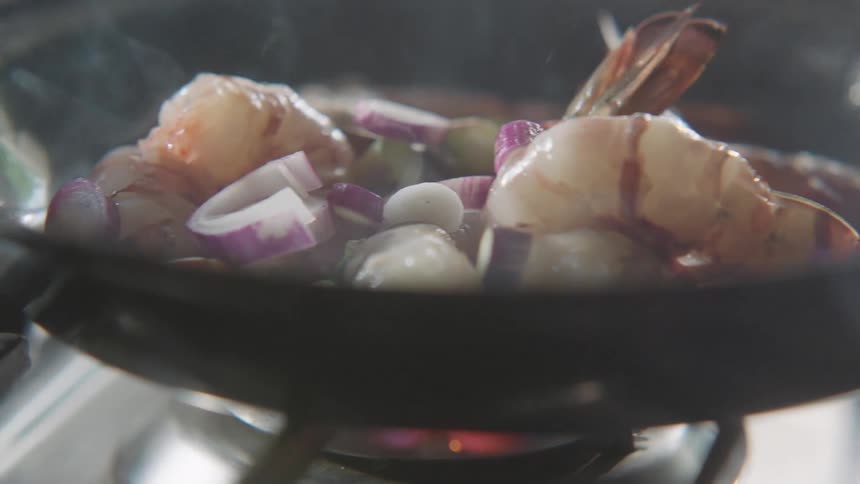 Vegetables are dropped into the pan to cook with the seafood