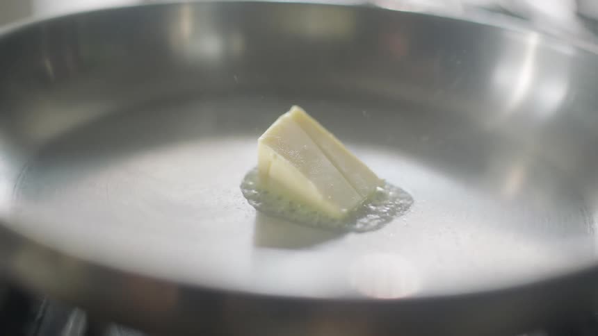Hand placing slice of butter on a hot pan or it to melt