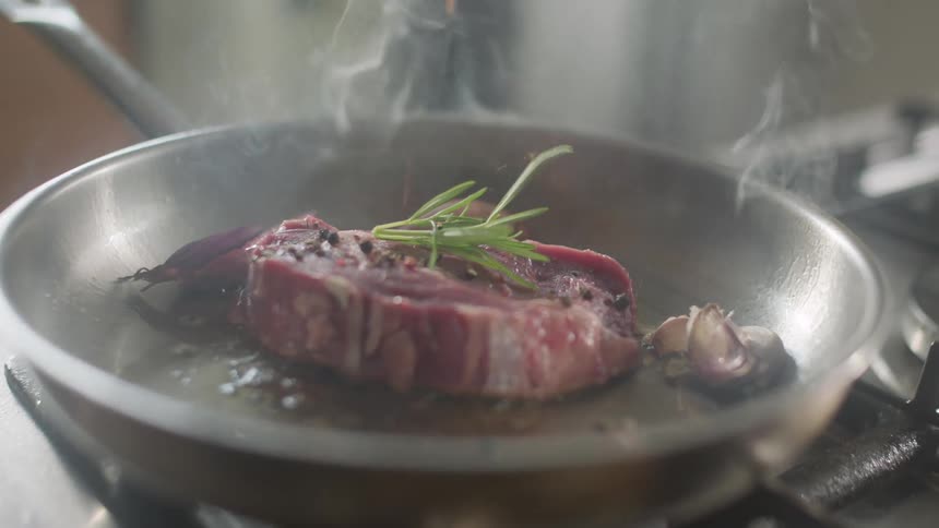 Steak cooking in a pan over a kitchen seasoned with herbs and pepper