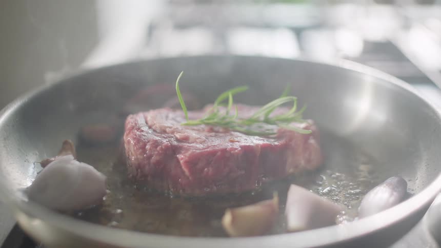 A steak and vegetables being fried in a skillet on atop an oven